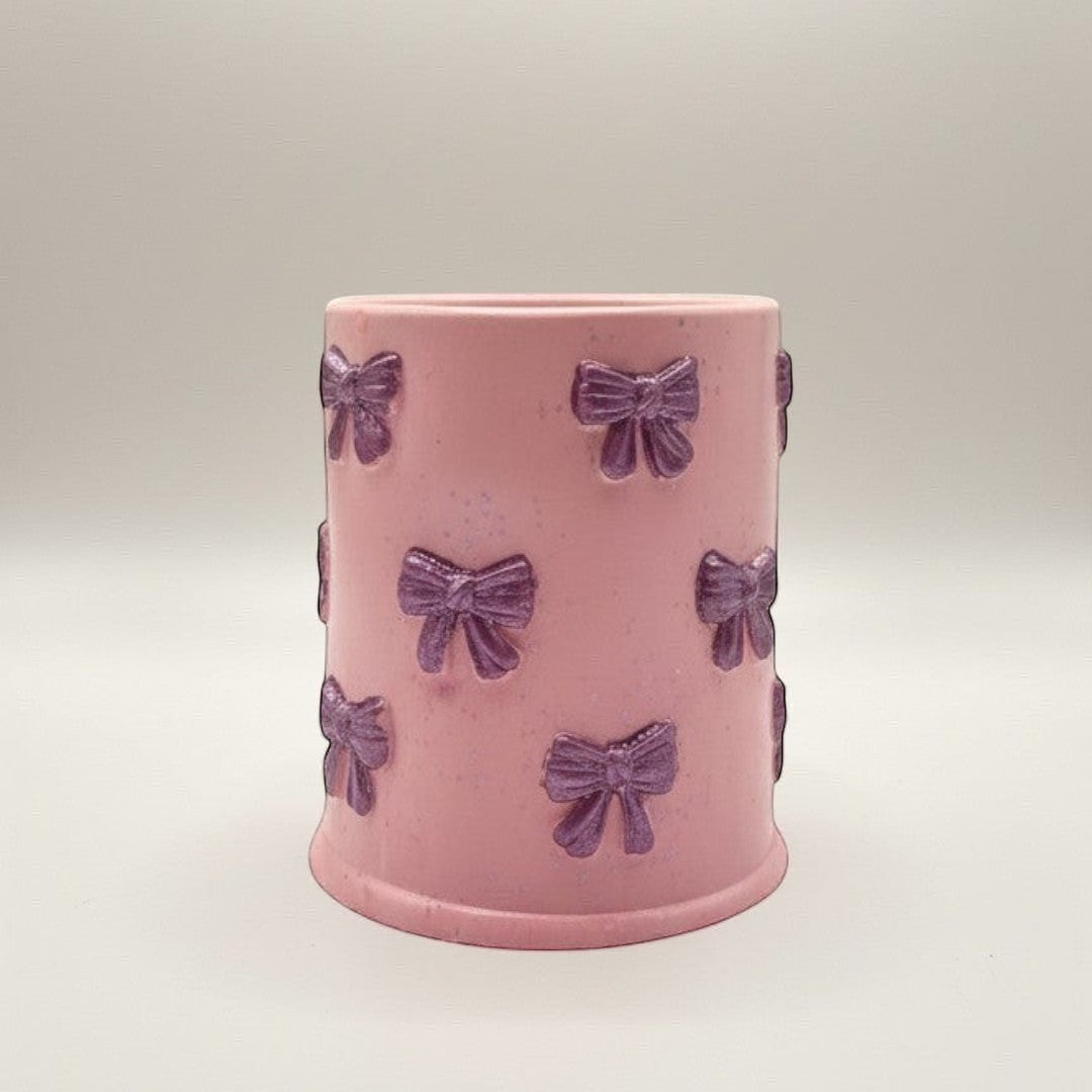 Doodlations Coffee Bar & Boutique pink concrete candle with purple bow accents and glitter flecks. 8oz soy blend wax.