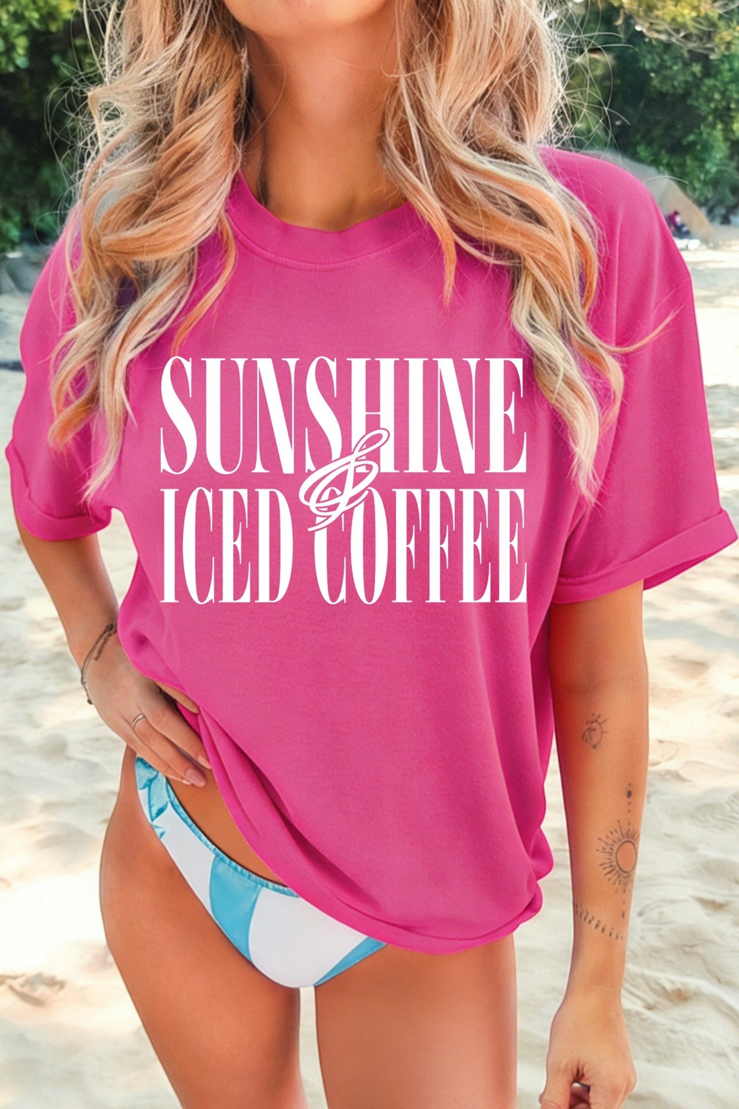 Doodlations Coffee Bar & Boutique hot pink crewneck t-shirt with white Sunshine And Iced Coffee graphic on a beach