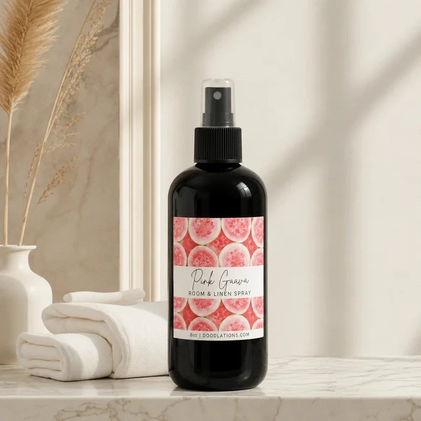Doodlations Coffee Bar & Boutique Pink Guava room and linen spray in a black bottle on a marble countertop.