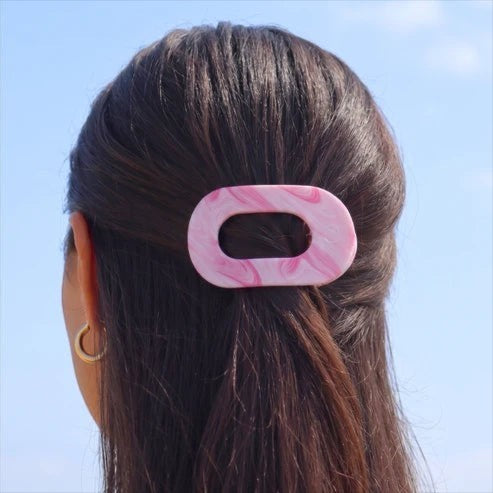 Doodlations Coffee Bar & Boutique pink and white marbled flat round hair clip worn in dark hair against a blue sky