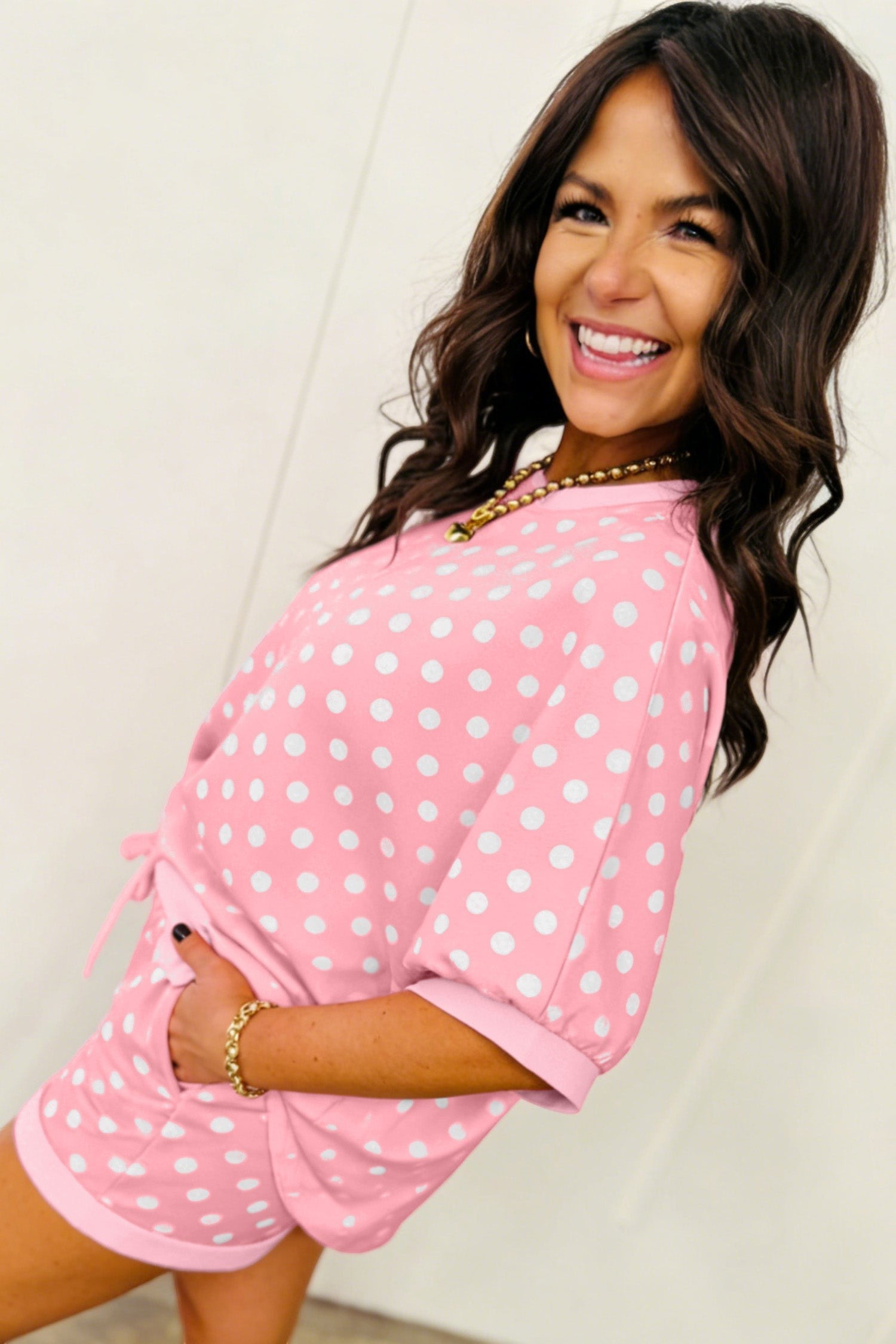 Woman smiling wearing a Doodlations Coffee Bar & Boutique pink and white polka dot lounge set with cuffed sleeves.
