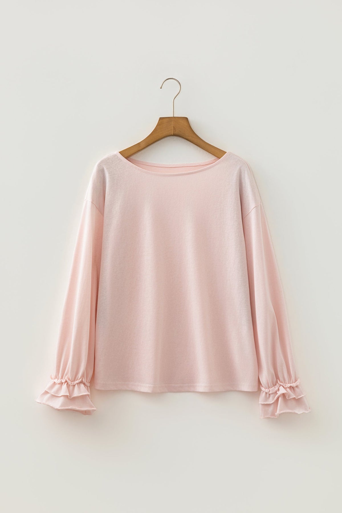 Doodlations Coffee Bar & Boutique baby pink long sleeve top with delicate ruffle cuffs on a wooden hanger.