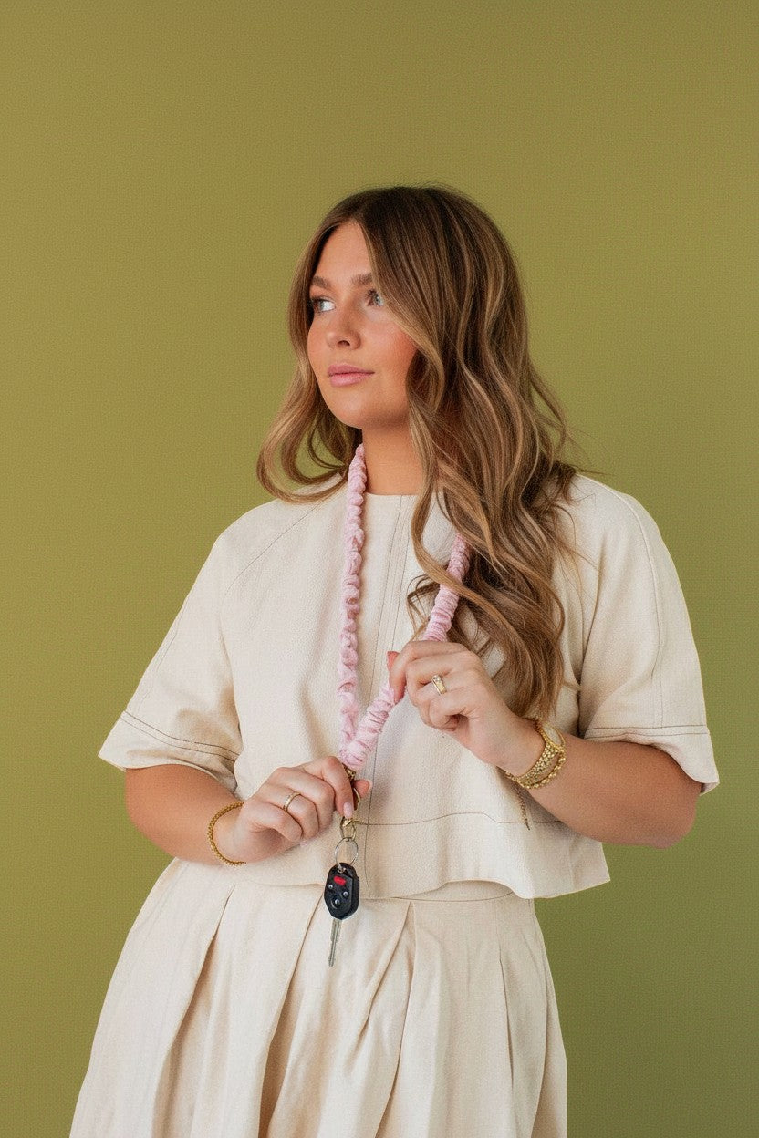 Doodlations Coffee Bar & Boutique light pink floral-textured fabric lanyard worn by a woman against a green backdrop