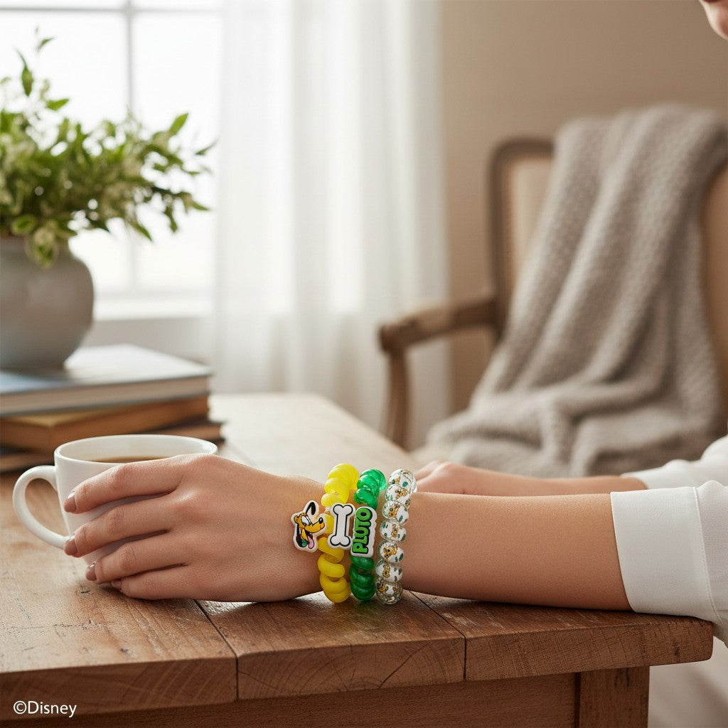 Doodlations Coffee Bar & Boutique Disney Pluto spiral hair ties worn as bracelets on a woman's wrist at a table.
