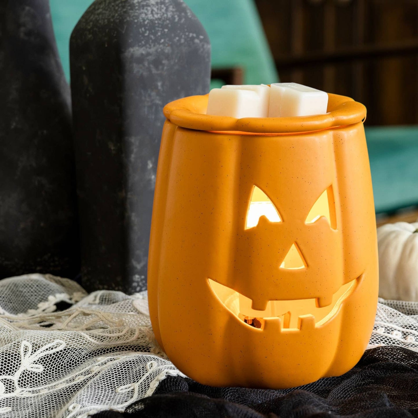 Doodlations Coffee Bar & Boutique orange ceramic Jack o' Lantern wax warmer with glowing face on a lace table runner