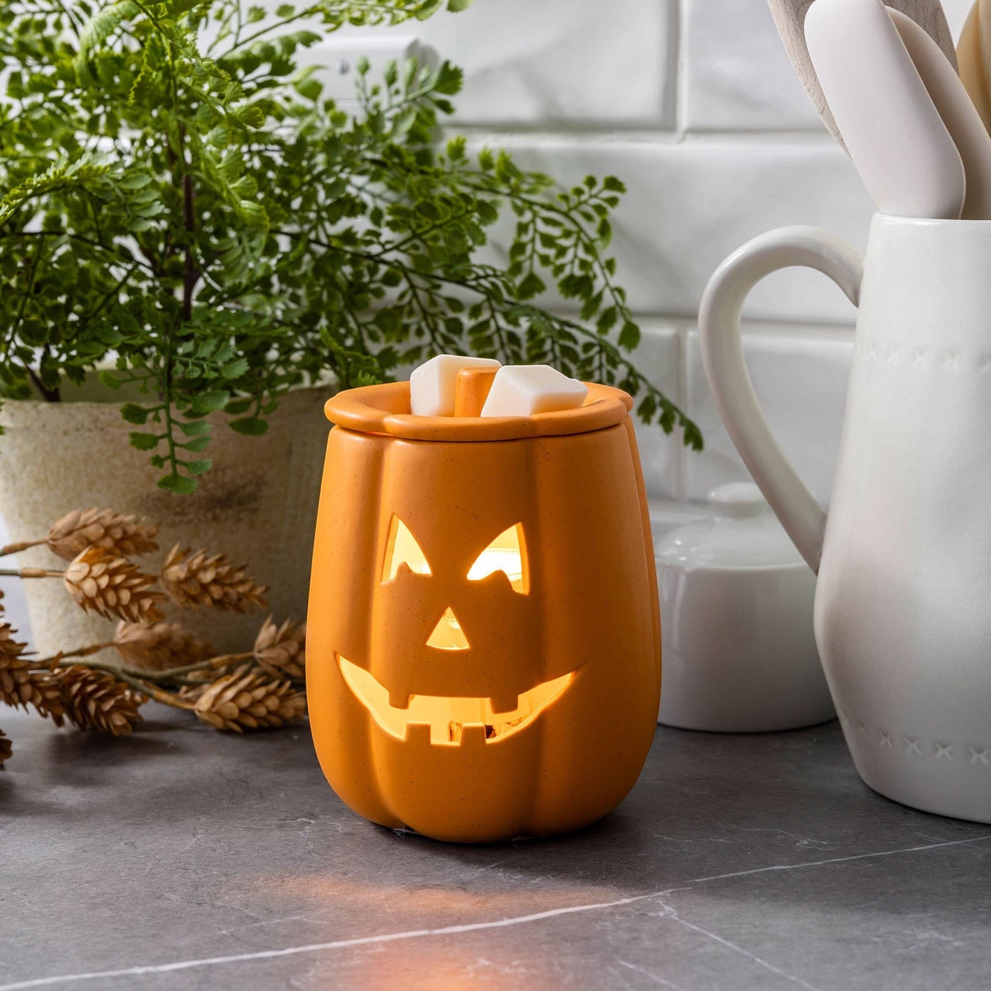 Doodlations Coffee Bar & Boutique orange ceramic Jack o' Lantern electric wax warmer with glowing face on counter