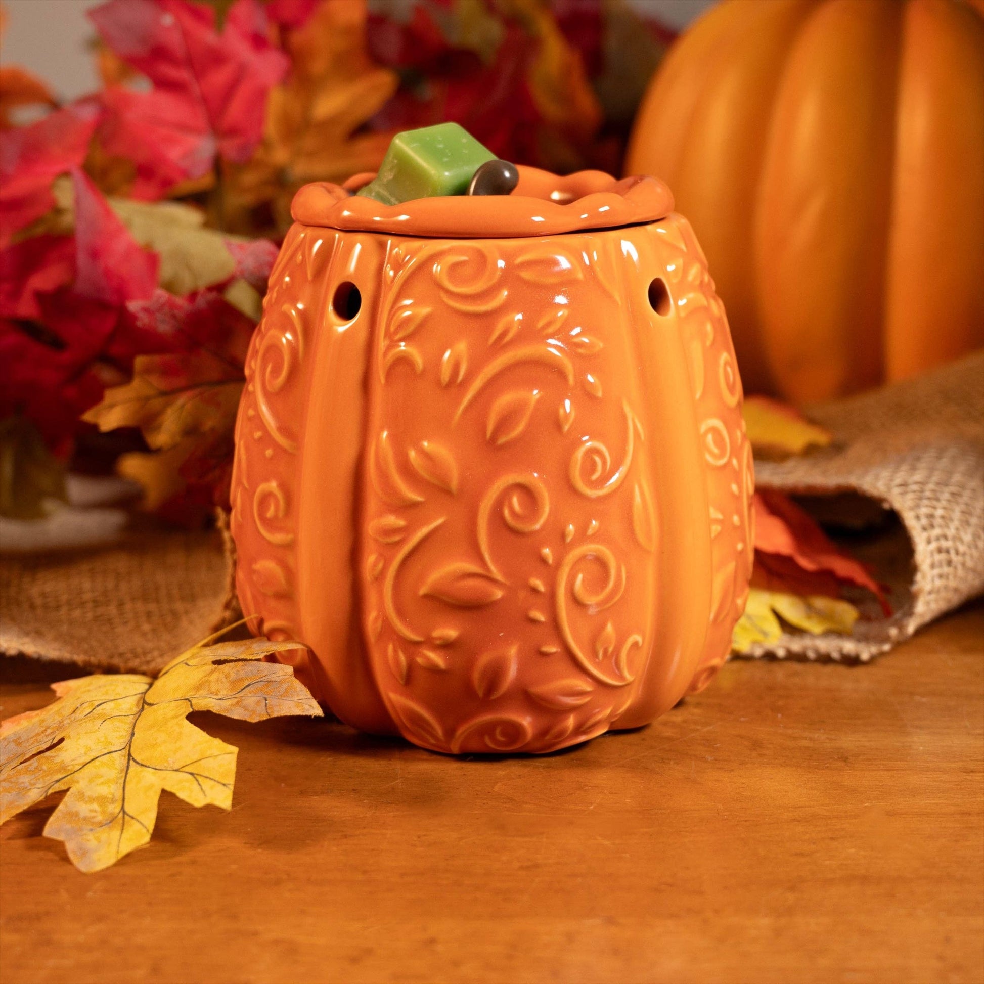 Doodlations Coffee Bar & Boutique orange ceramic pumpkin wax warmer with embossed scrollwork on a wooden table.