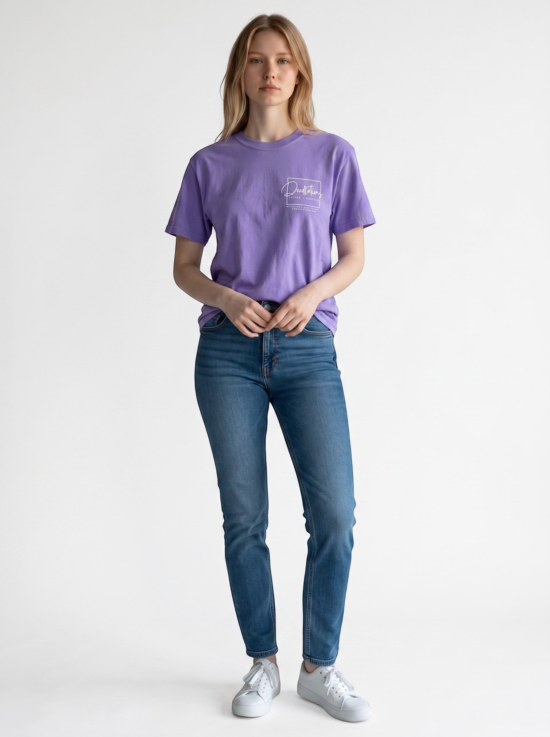 Model wearing a purple Doodlations Coffee Bar & Boutique graphic tee with a white logo, paired with blue jeans.