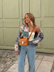 Woman wearing a Doodlations Coffee Bar & Boutique quilted patchwork floral jacket with jeans and a tan crossbody bag