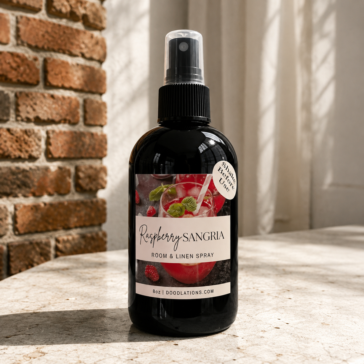 Doodlations Coffee Bar & Boutique Raspberry Sangria room and linen spray in a black bottle on a stone surface.
