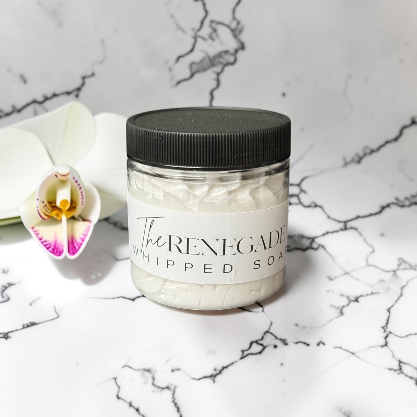 Doodlations Coffee Bar & Boutique The Renegade whipped soap in a clear jar with black lid on a marble surface.