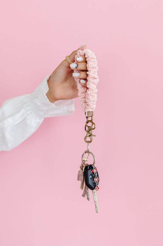 Doodlations Coffee Bar & Boutique rose corduroy scrunchie keychain held on a wrist against a pink background