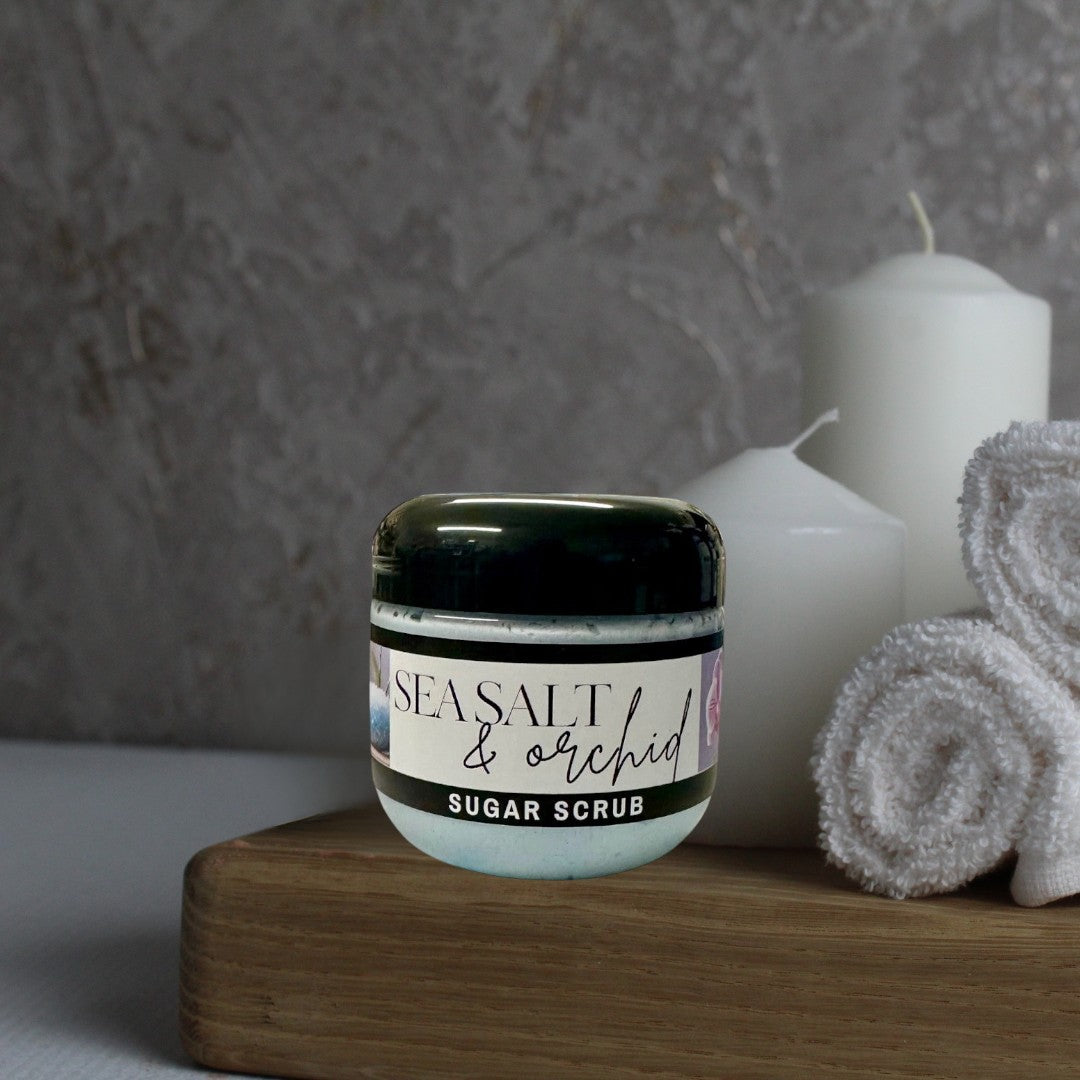 Doodlations Coffee Bar & Boutique Sea Salt & Orchid Sugar Scrub in a clear jar with a black lid, light blue scrub inside.