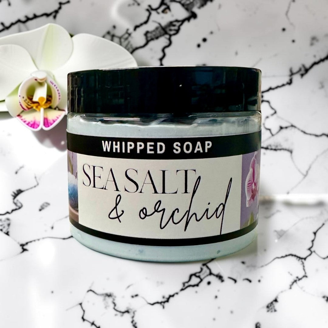 Doodlations Coffee Bar & Boutique Sea Salt & Orchid whipped soap in a jar sitting in blue water with ripples.