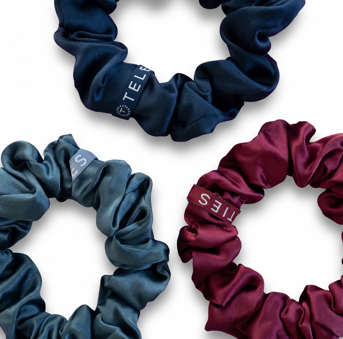 Doodlations Coffee Bar & Boutique Teleties silk scrunchies in navy, burgundy, and steel blue with inner coil grip.