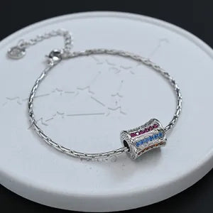 Doodlations Coffee Bar & Boutique silver-plated chain bracelet featuring a cylindrical charm with red and blue stones.