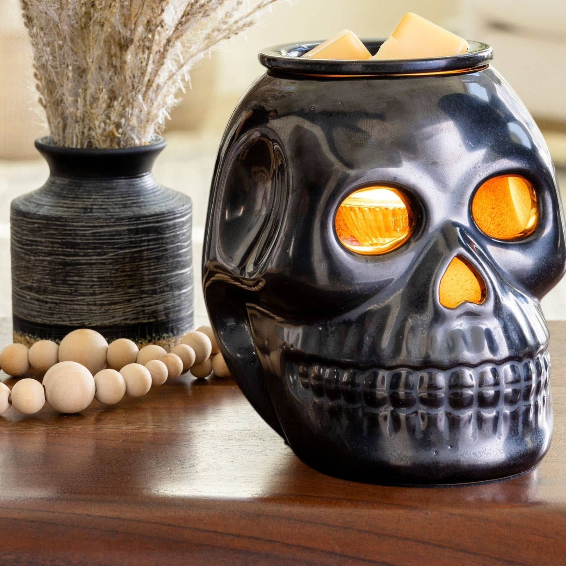 Doodlations Coffee Bar & Boutique gunmetal skull fragrance warmer with glowing eyes and wax melts on a wooden table.
