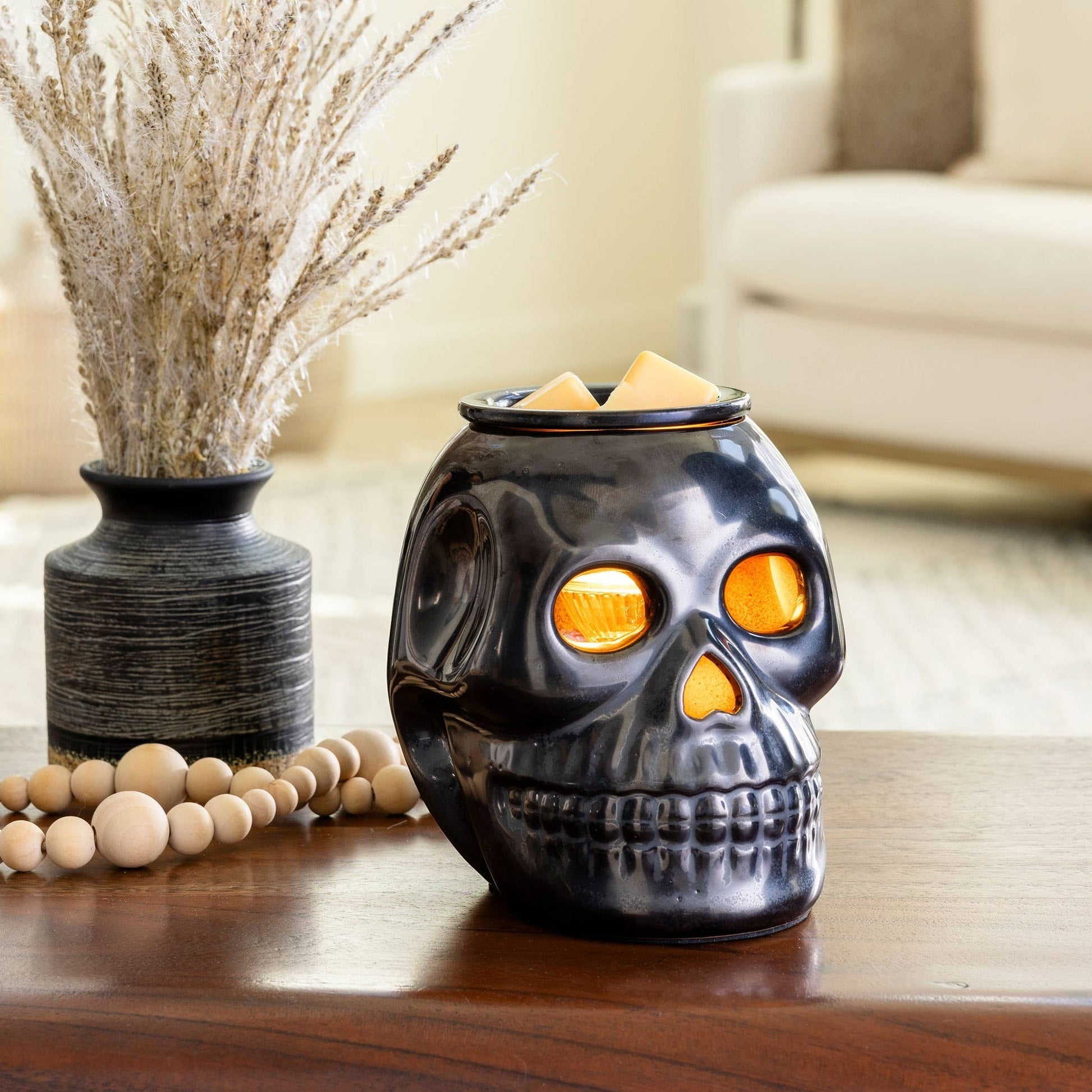 Doodlations Coffee Bar & Boutique gunmetal skull fragrance warmer with glowing eyes and wax melts on a wooden table.
