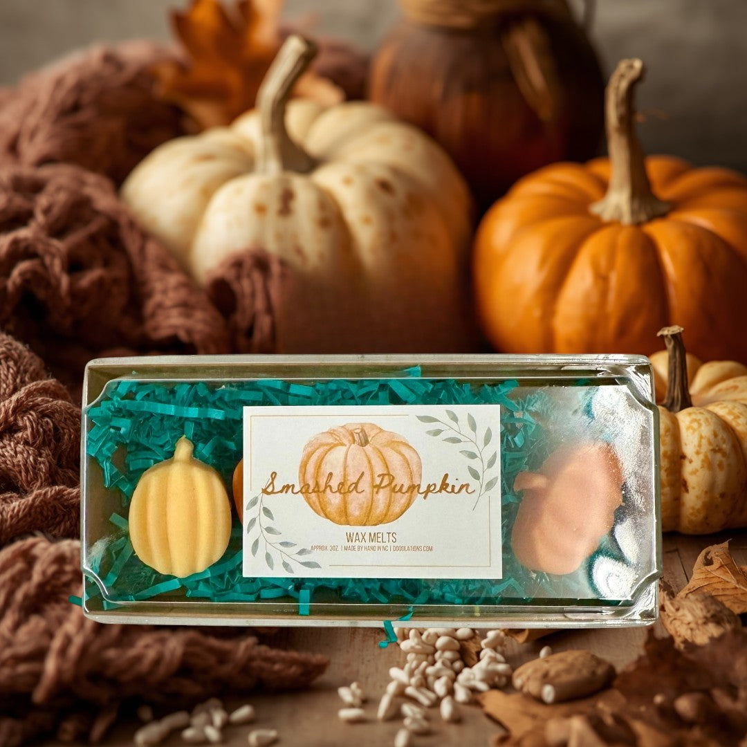 Doodlations Smashed Pumpkin wax melts in a clear box with teal crinkle paper. Two pumpkin-shaped wax melts are visible.