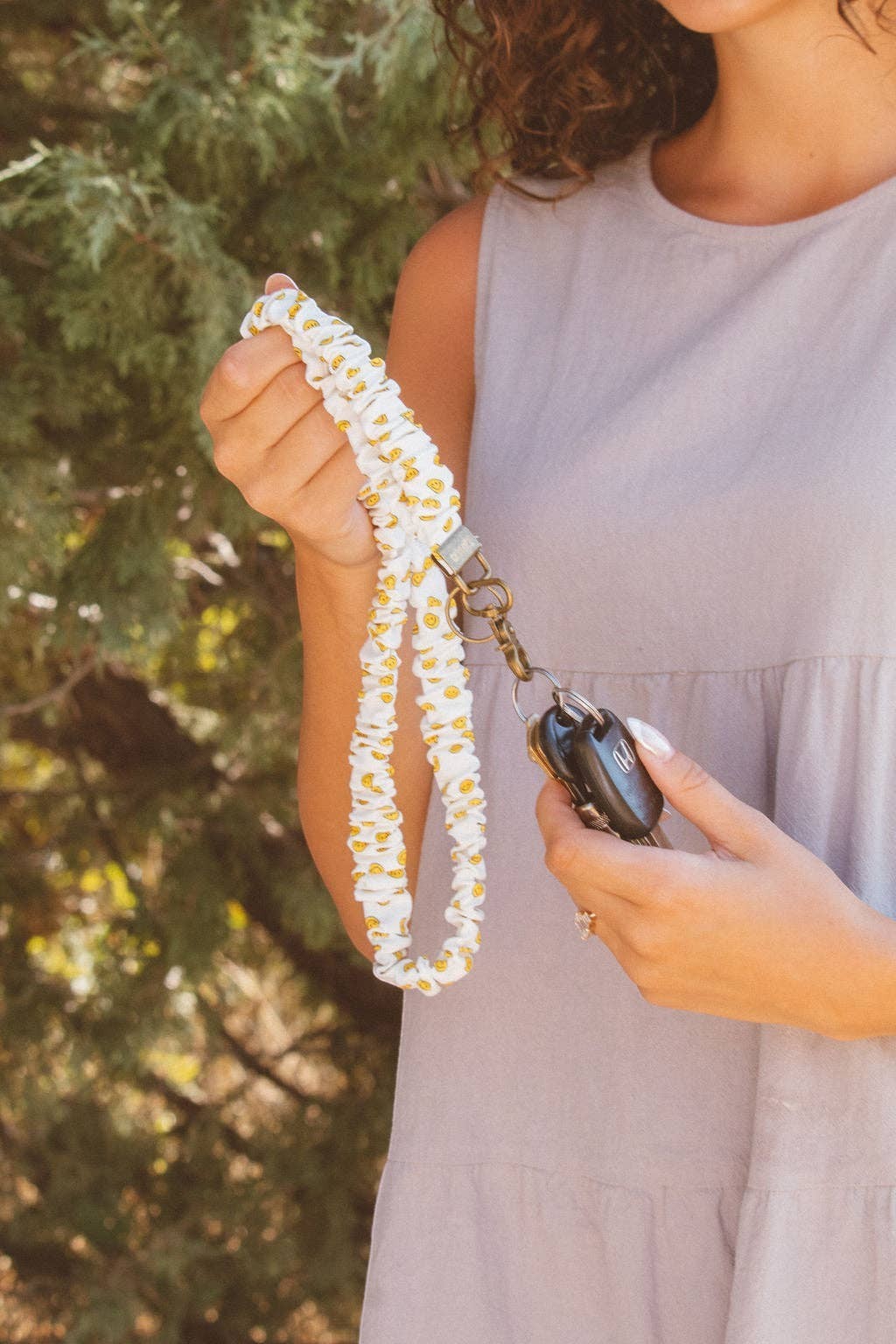 Doodlations Coffee Bar & Boutique white luxe fabric lanyard with yellow smiley face pattern holding car keys