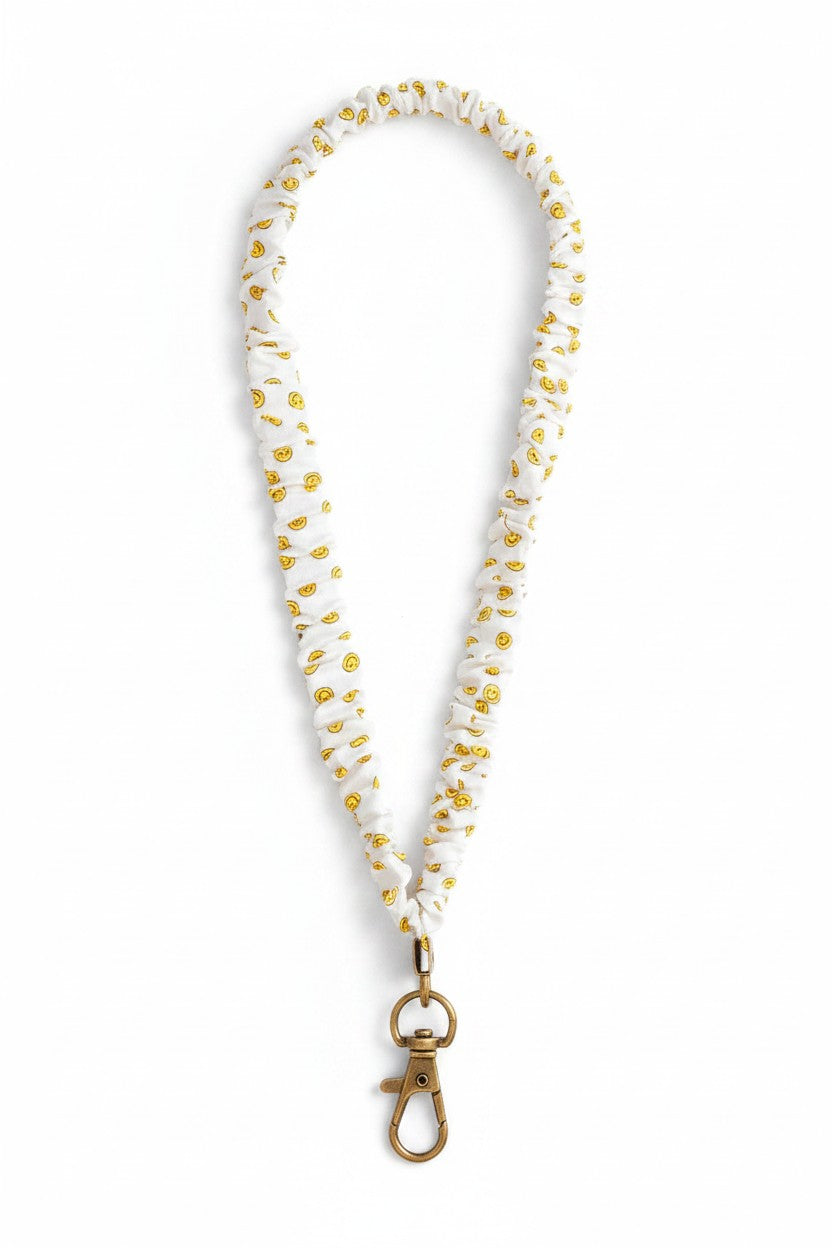 Doodlations Coffee Bar & Boutique white luxe fabric lanyard featuring a yellow smiley face pattern and brass clasp.