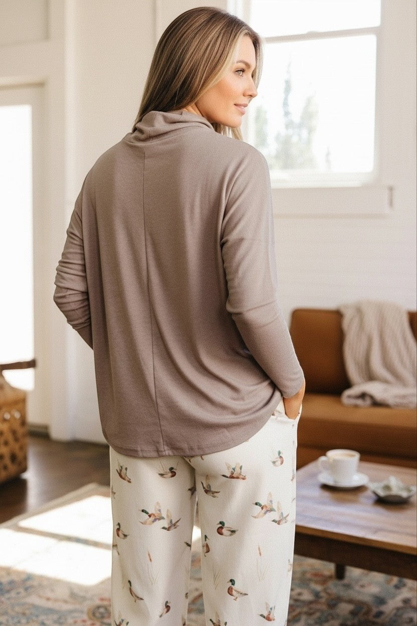 Doodlations Coffee Bar & Boutique smoke gray high neck long sleeve top worn by a woman with hands in pockets