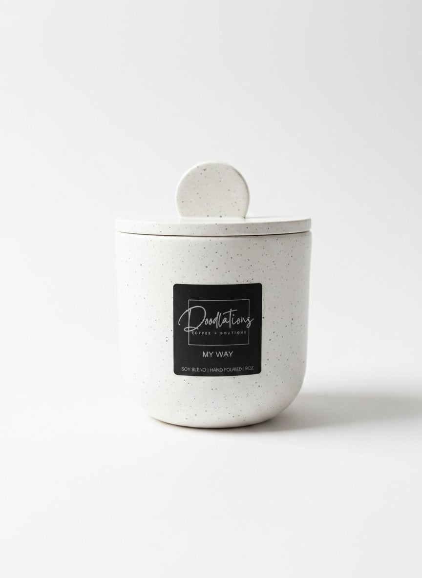 Doodlations Coffee Bar & Boutique white speckled concrete candle with a matching lid and black label on a white background