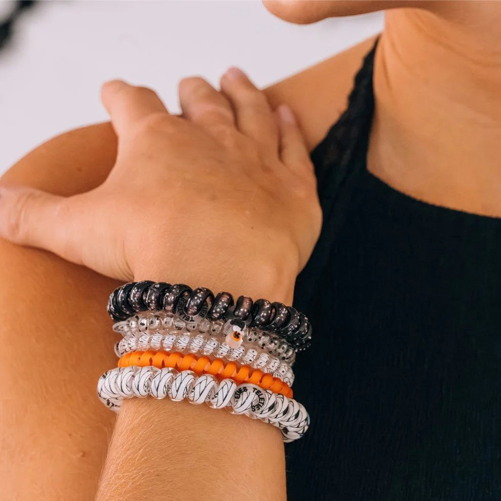 Doodlations Coffee Bar & Boutique spiral hair ties in black, orange, and clear worn as a bracelet on a woman's wrist