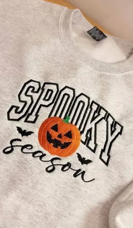 Doodlations Coffee Bar & Boutique grey unisex sweatshirt with embroidered Spooky Season text and pumpkin design.