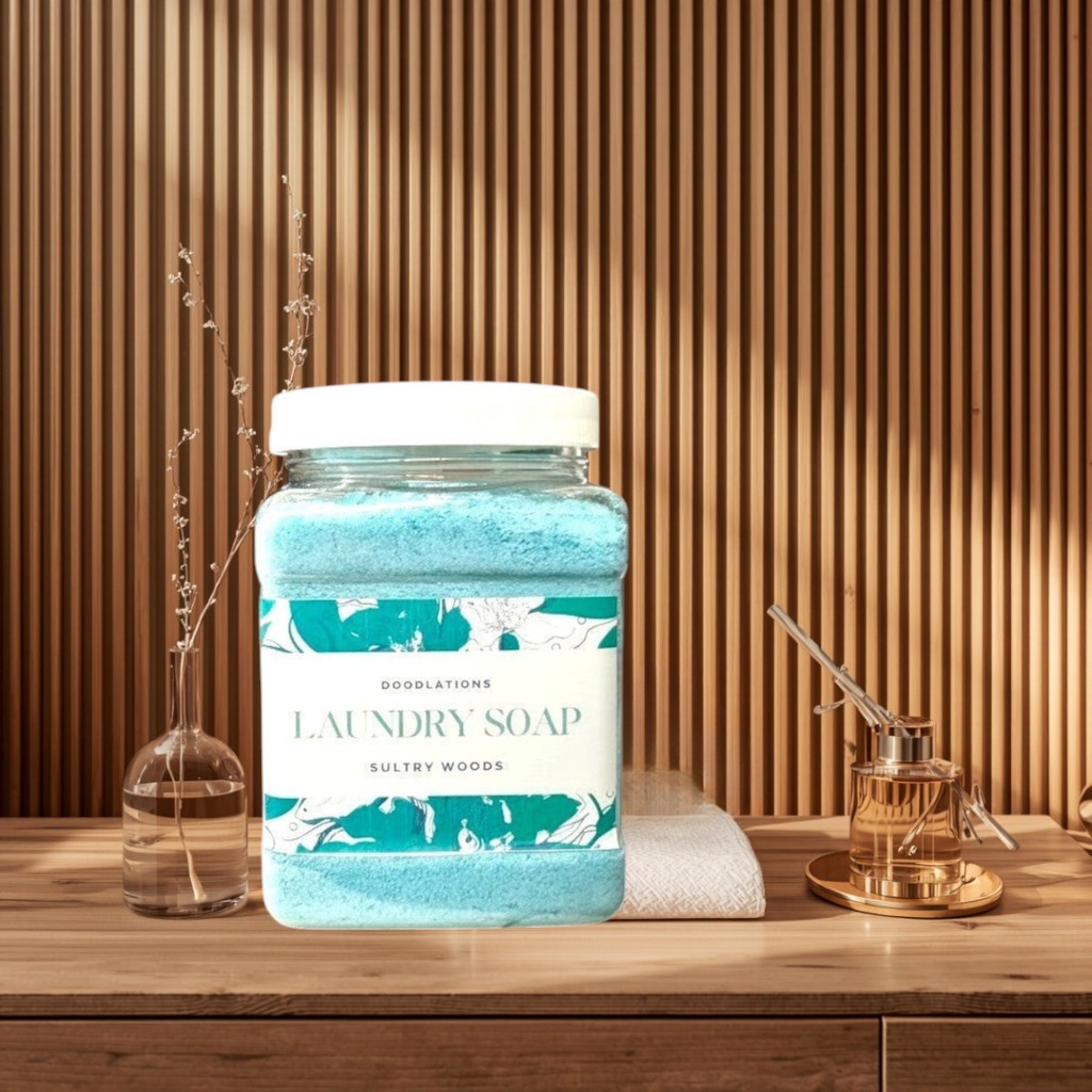 Doodlations Coffee Bar & Boutique Sultry Woods powdered laundry detergent in a clear jar with a white lid. Blue powder fills the jar.