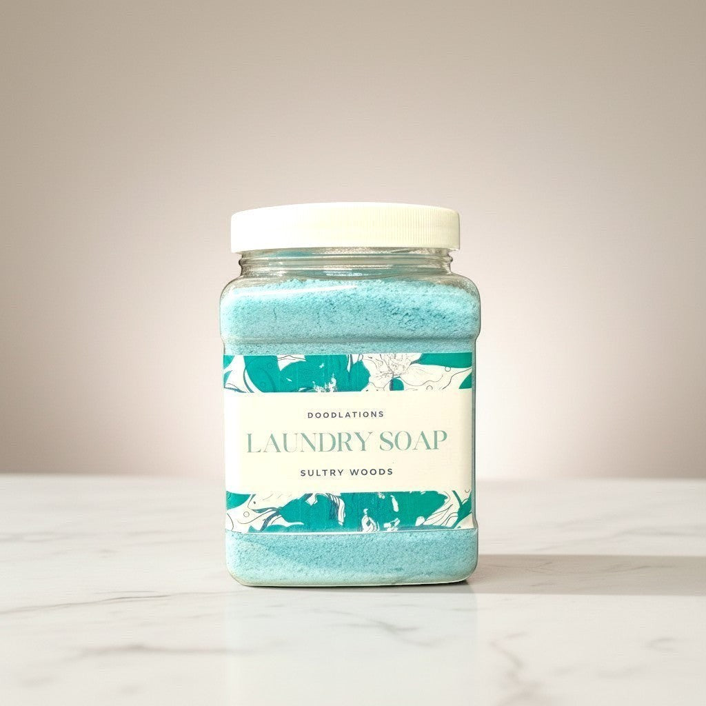Doodlations Coffee Bar & Boutique Sultry Woods powdered laundry soap in a clear jar with a white lid. Blue powder fills the jar.