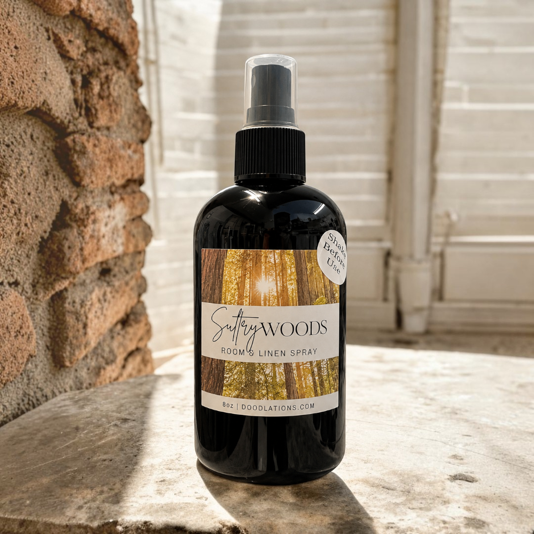 Doodlations Coffee Bar & Boutique Sultry Woods room and linen spray in a black bottle on a stone surface