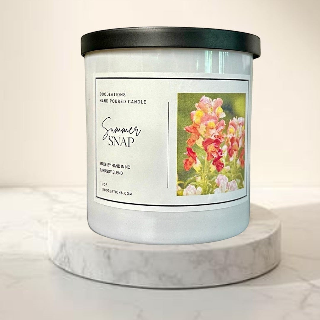 Doodlations Coffee Bar & Boutique Summer Snap hand-poured parasoy blend candle with floral-fruity scent. White jar, black lid.