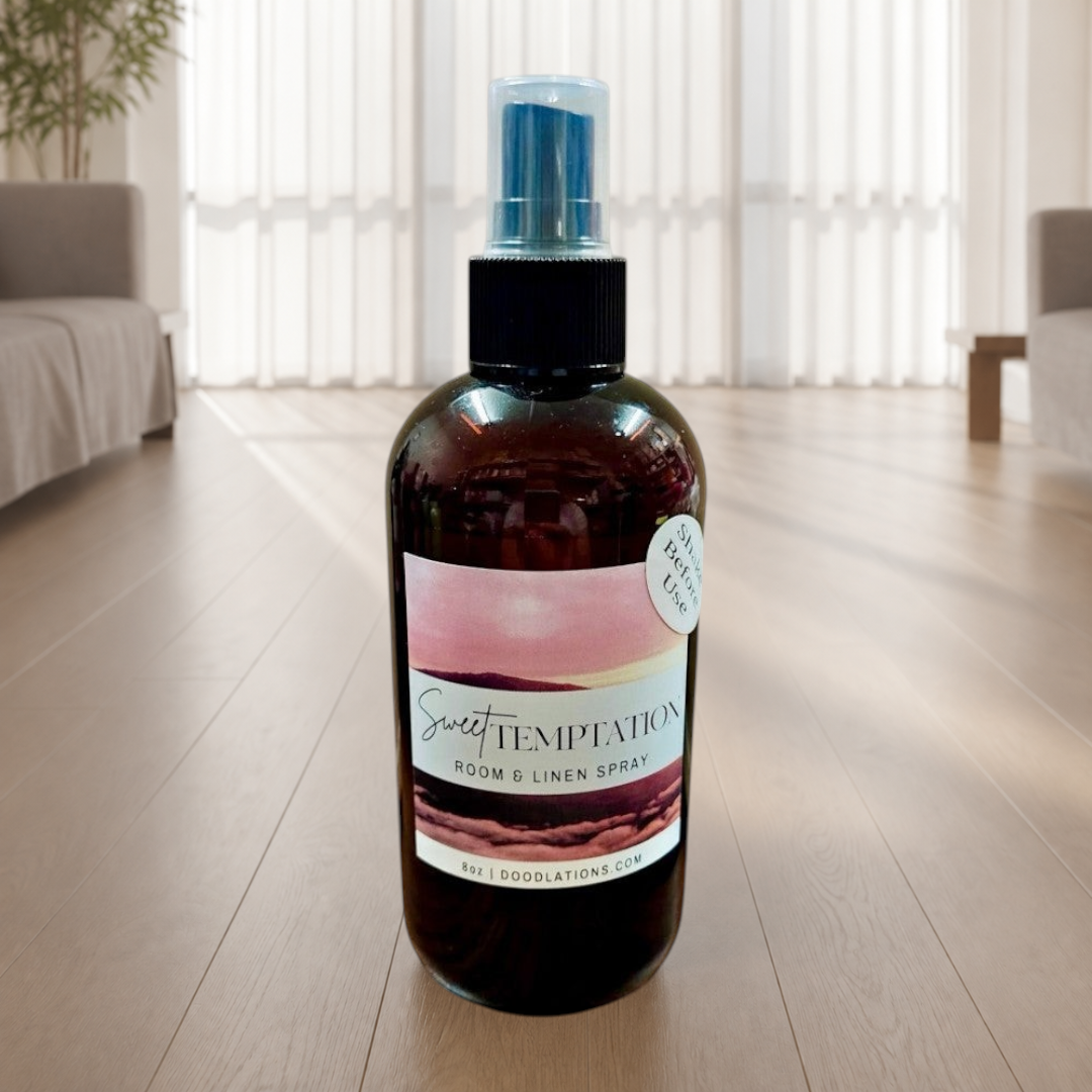 Doodlations Coffee Bar & Boutique Sweet Temptation room and linen spray in an amber bottle on a wooden floor.