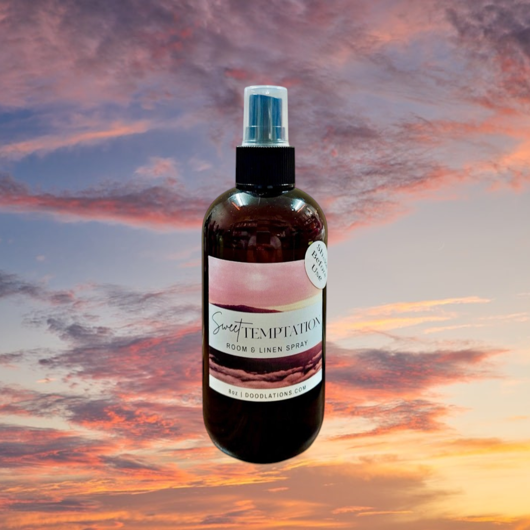 Doodlations Coffee Bar & Boutique Sweet Temptation room and linen spray in an amber bottle against a sunset sky