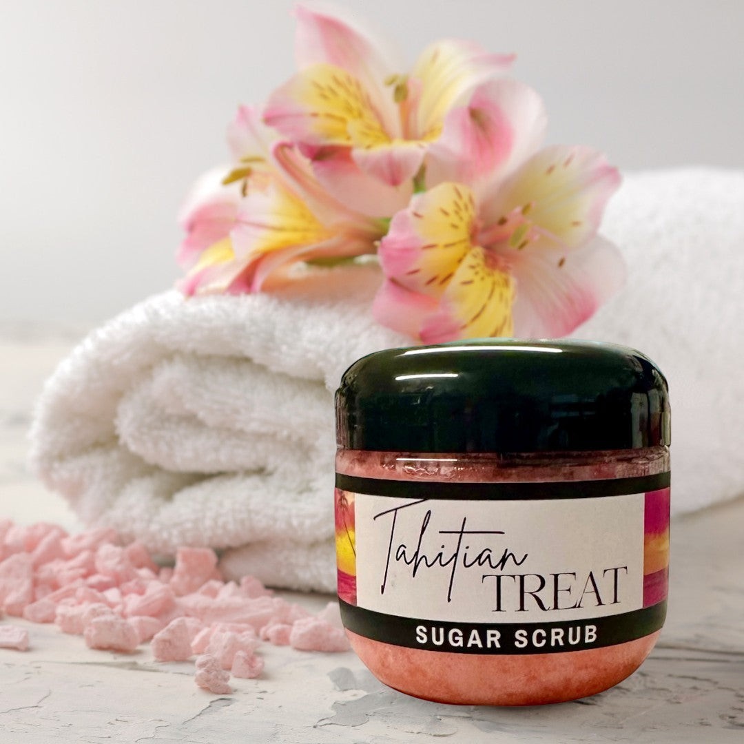 Doodlations Coffee Bar & Boutique Tahitian Treat Sugar Scrub, a pink exfoliating body scrub in a clear jar with a black lid, set against a blue water background.