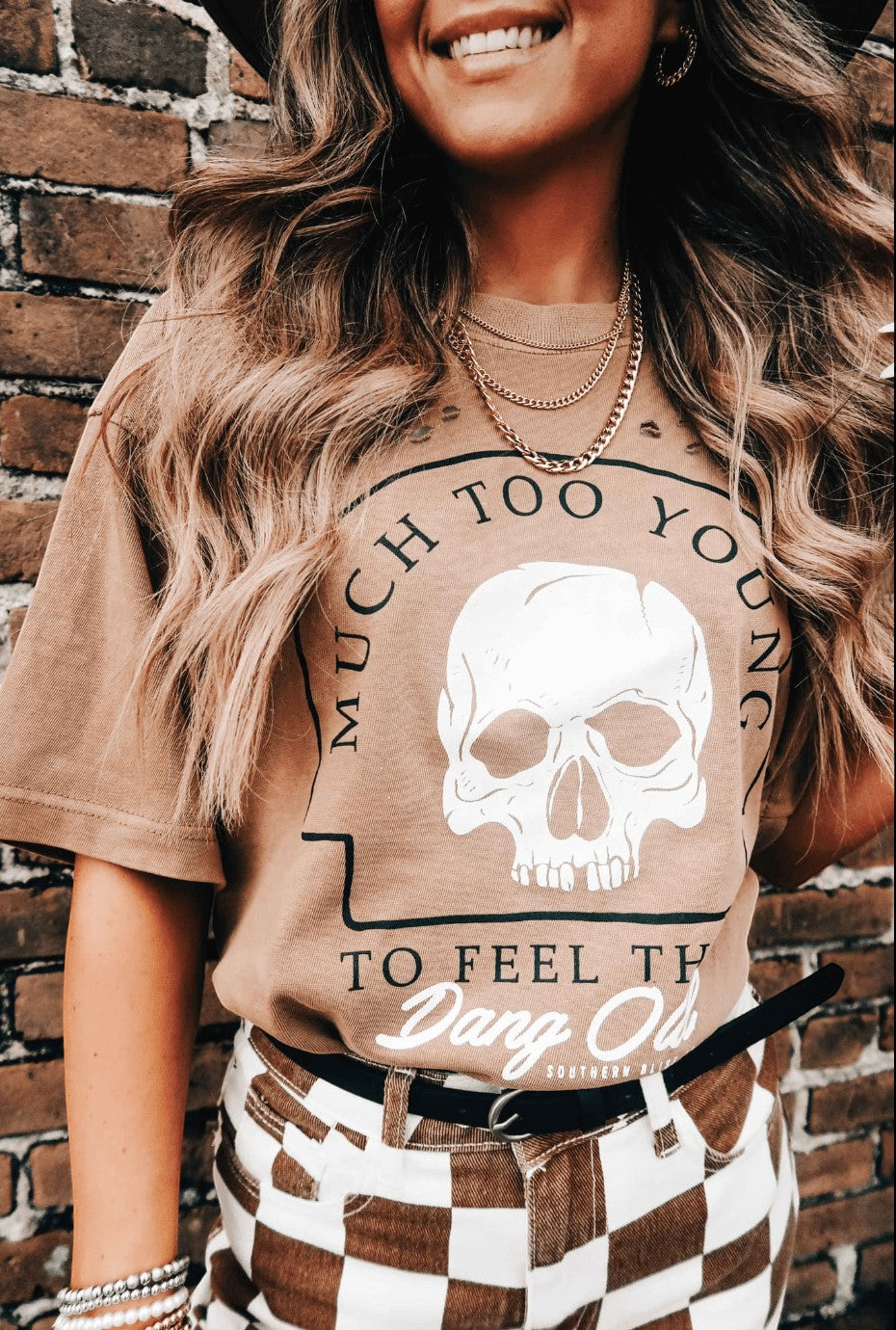 Doodlations Coffee Bar & Boutique tan graphic t-shirt with skull print and text worn with checkered pants