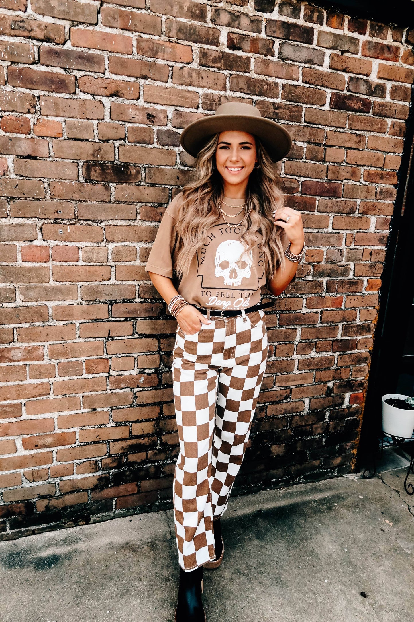 Doodlations Coffee Bar & Boutique tan graphic skull t-shirt worn by a woman with a hat and checkered pants