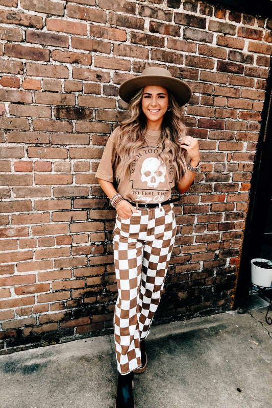 Doodlations Coffee Bar & Boutique tan graphic skull t-shirt worn by a woman with a hat and checkered pants