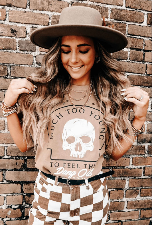 Doodlations Coffee Bar & Boutique tan graphic skull t-shirt worn by a woman in a hat and checkered pants