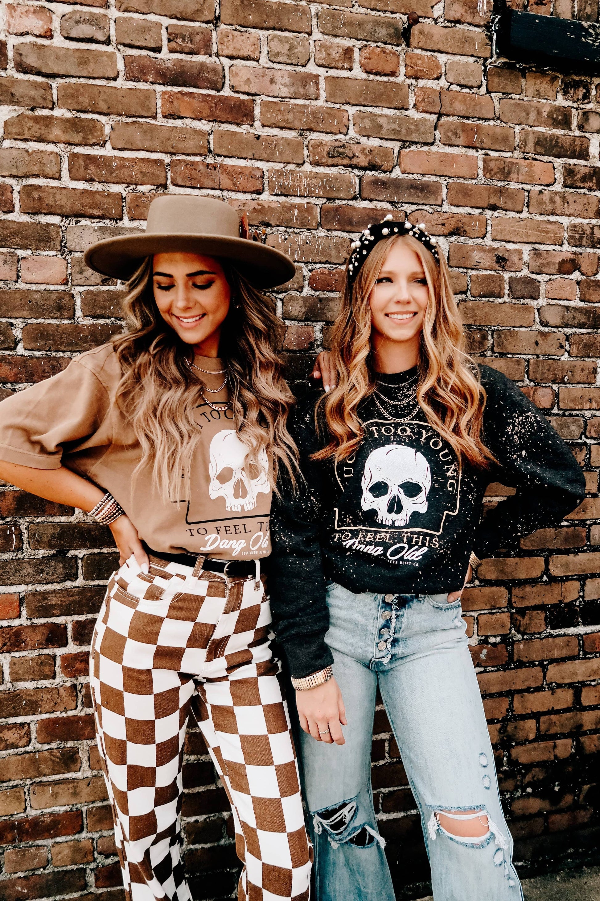Doodlations Coffee Bar & Boutique tan graphic skull t-shirt worn by a woman with a hat against a brick wall