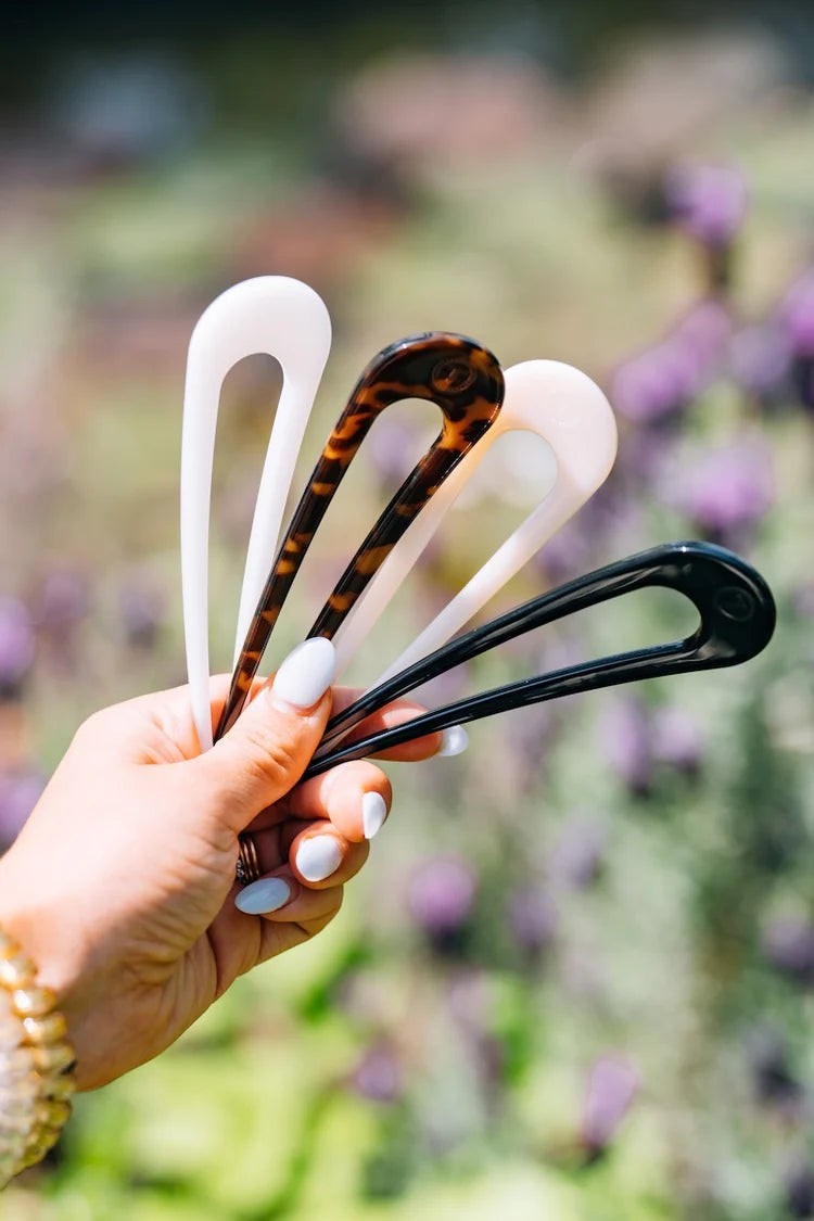Doodlations Coffee Bar & Boutique Teleties French hair pins in white, tortoise, and black held in a hand outdoors.