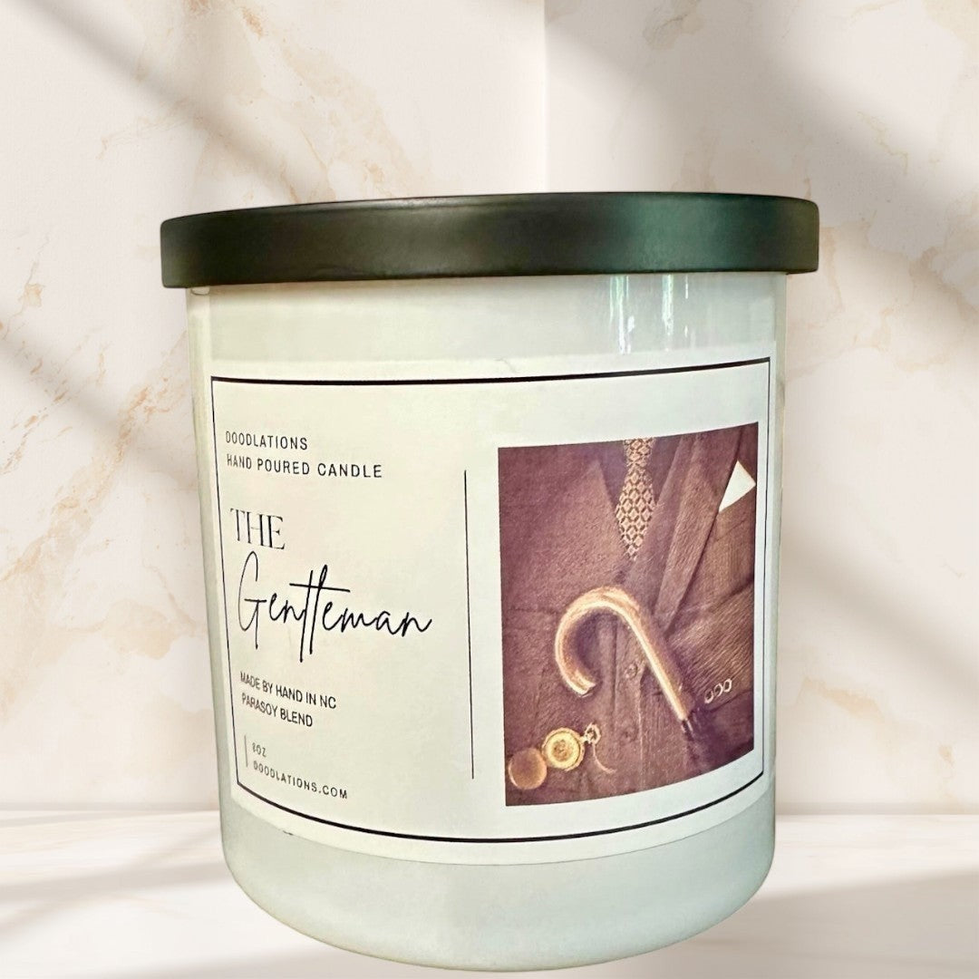 Doodlations Coffee Bar & Boutique The Gentleman hand-poured soy blend candle with masculine cologne scent. White jar with black lid.