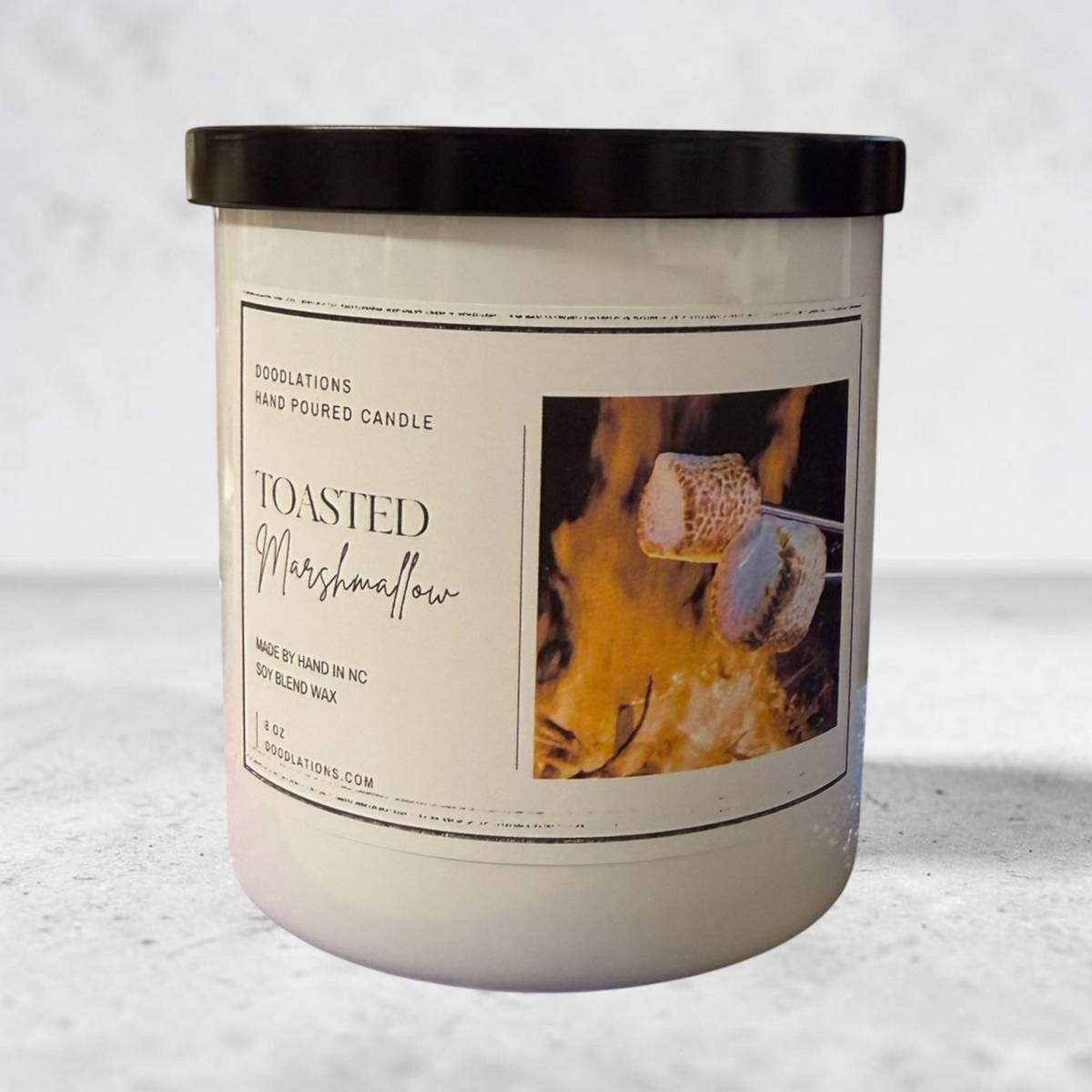 Doodlations Coffee Bar & Boutique Toasted Marshmallow scented soy blend candle in a white jar with a black lid.