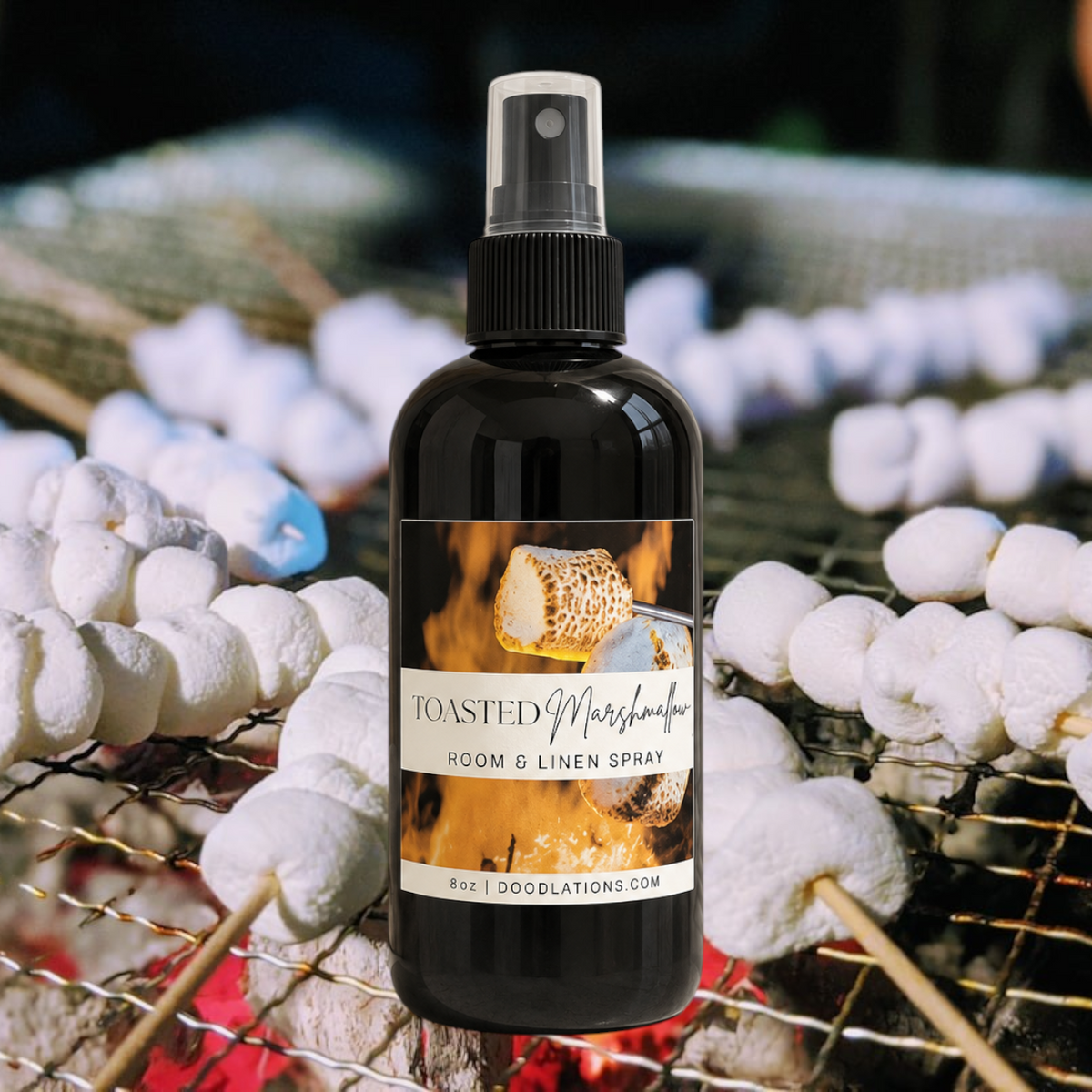 Doodlations Coffee Bar & Boutique Toasted Marshmallow room and linen spray in a black bottle over a campfire background