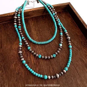 Doodlations Coffee Bar & Boutique layered statement necklace with turquoise beads and metallic accents on a wood tray