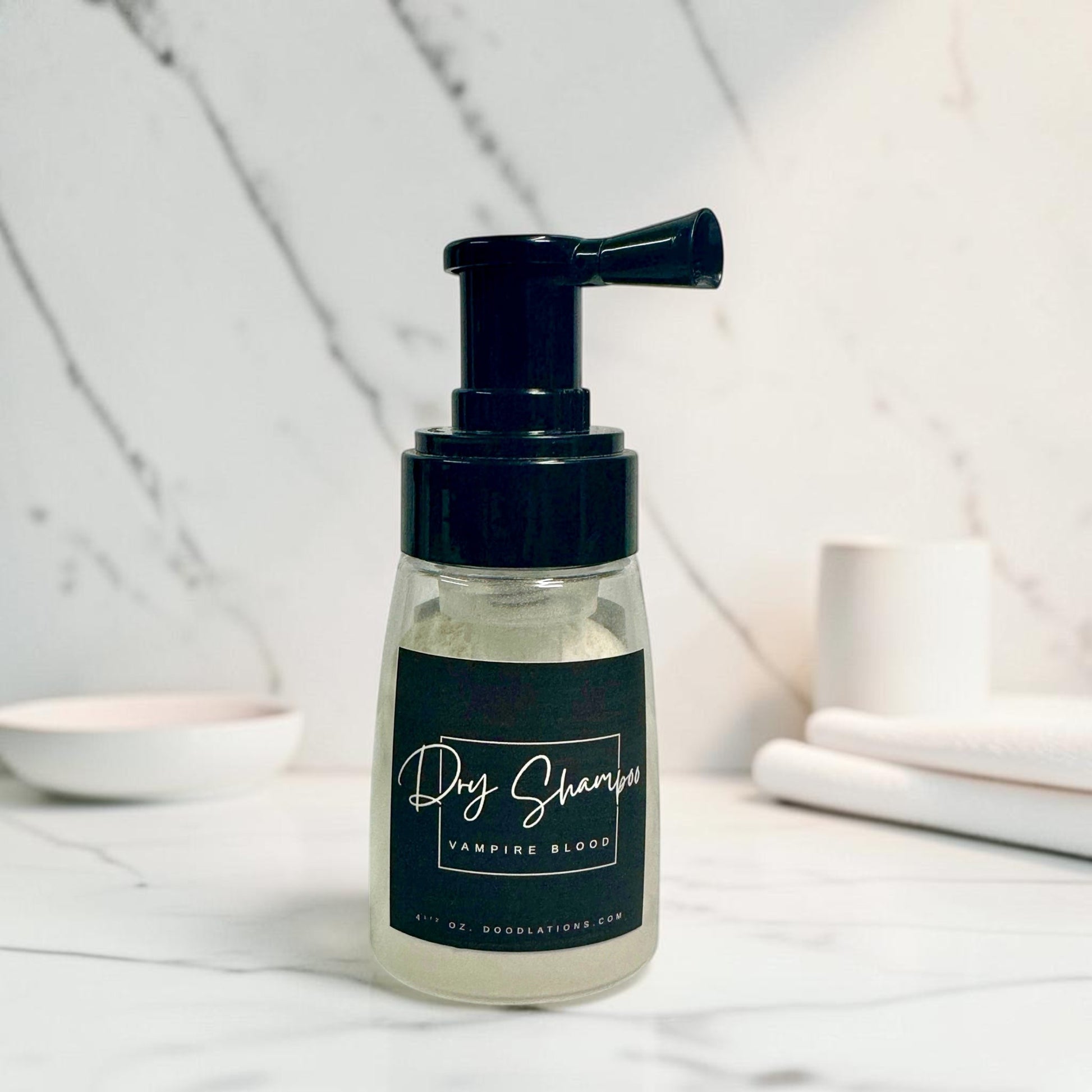 Doodlations Coffee Bar & Boutique Vampire Blood dry powder shampoo in a clear pump bottle on a marble surface.