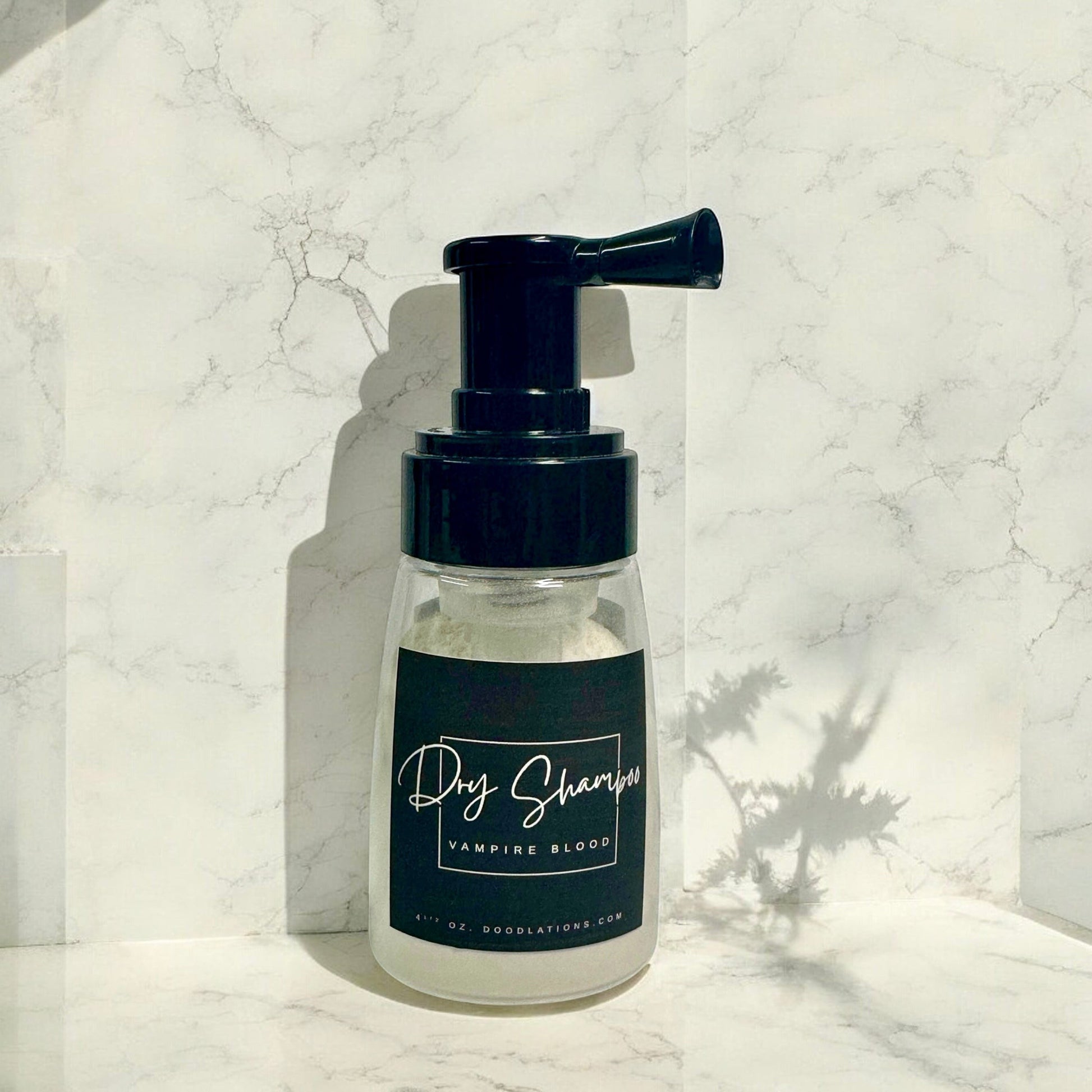 Doodlations Coffee Bar & Boutique Vampire Blood dry powder shampoo in a clear pump bottle against a marble background.
