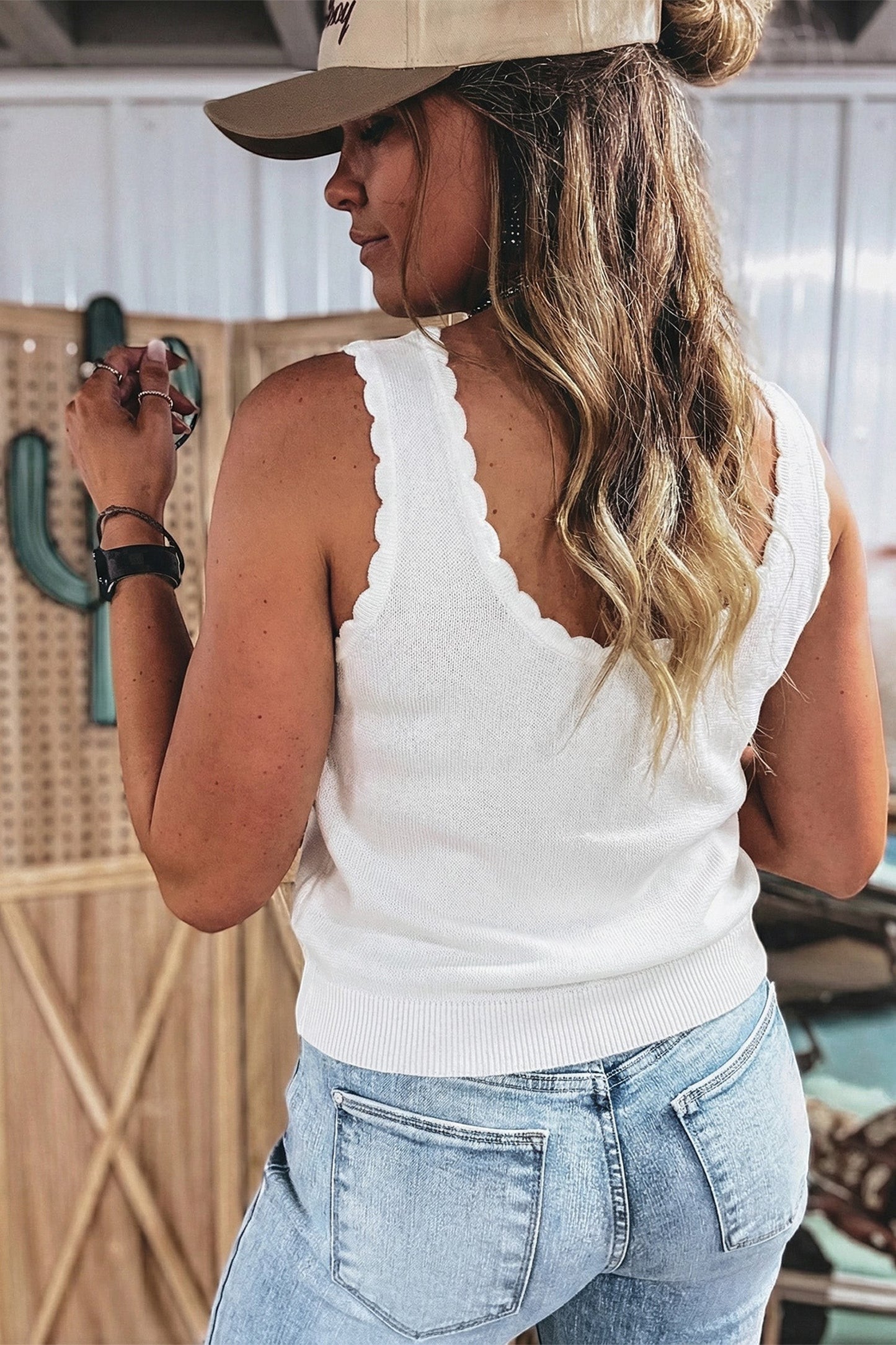 Doodlations Coffee Bar & Boutique white knit tank top with scalloped trim worn by a woman in jeans and a baseball cap