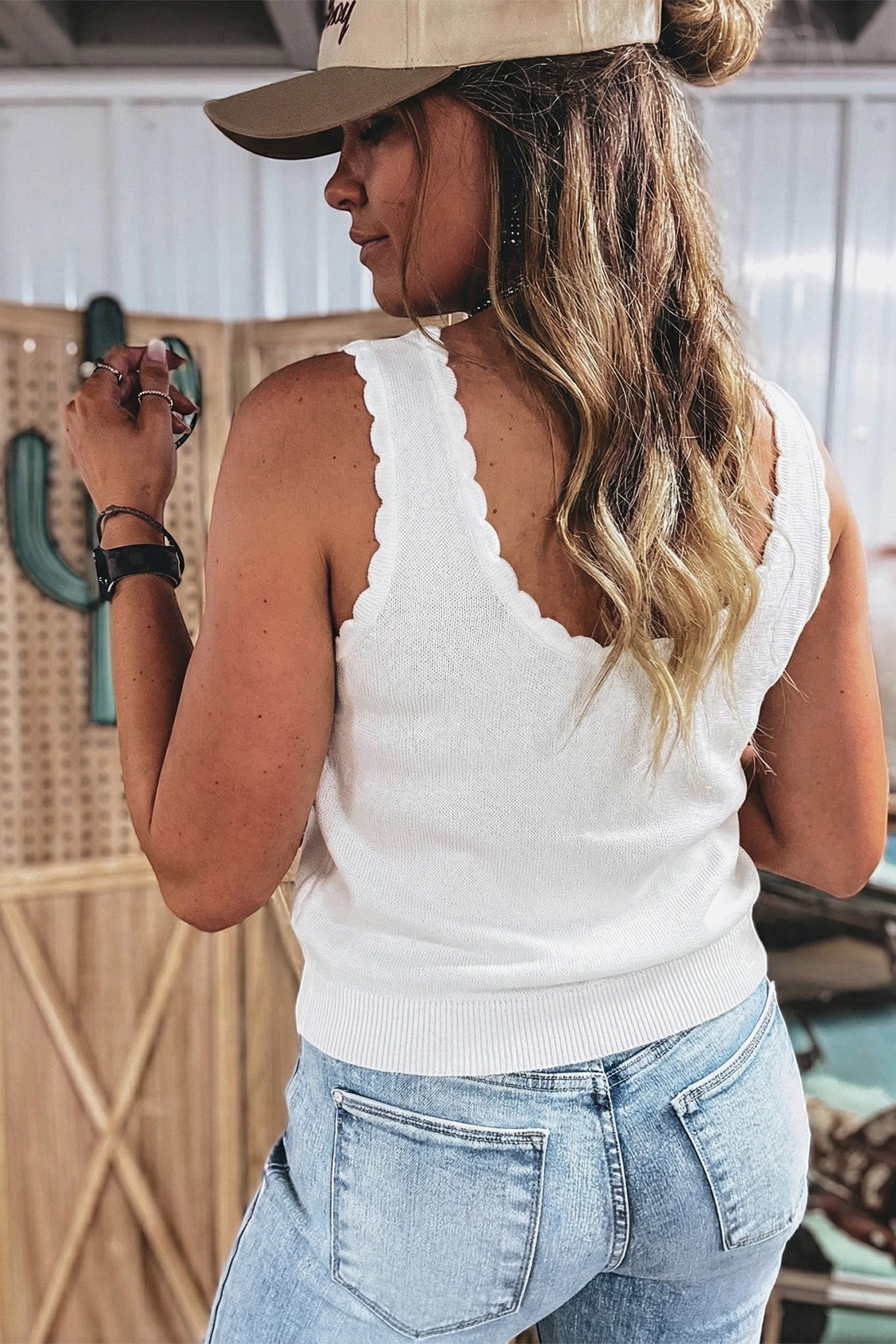 Doodlations Coffee Bar & Boutique white knit tank top with scalloped trim worn by a woman in jeans and a baseball cap